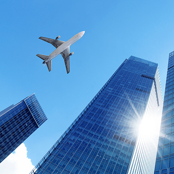 A jumbo jet airplane flying over skyscrapers. Clear blue sky behind.
